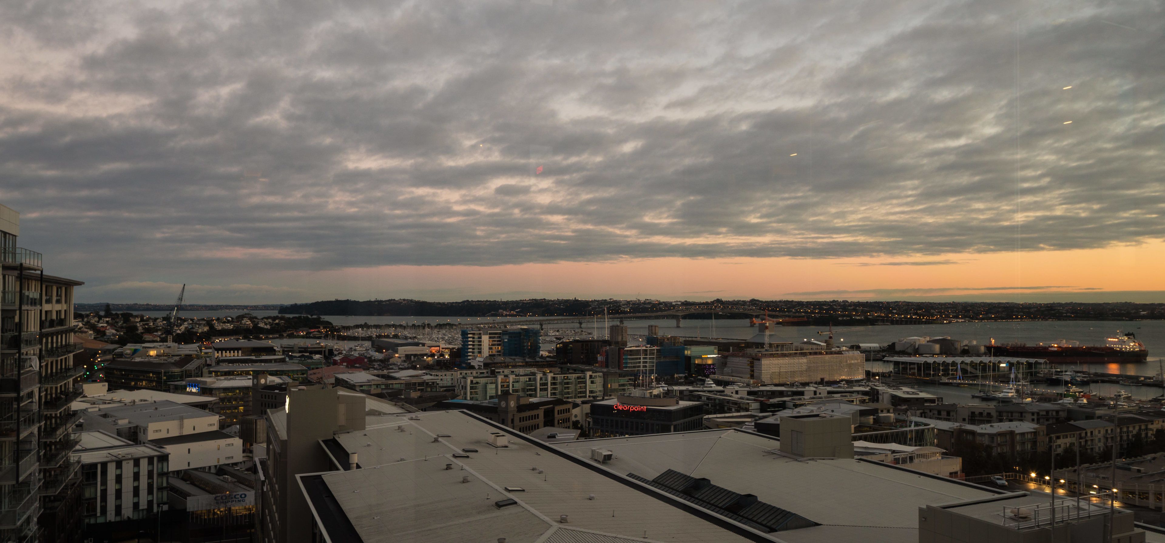 A cityscape at dusk with a view of the waterfront, buildings, and a bridge.