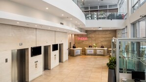 A modern hotel lobby with a reception desk, elevators, and a glass railing overlooking the lower level. - Rydges Auckland (Auckland)
