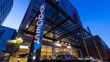 A hotel with a prominent 'RYDGES' sign, modern architecture, and a bar/lounge area visible through the glass facade.