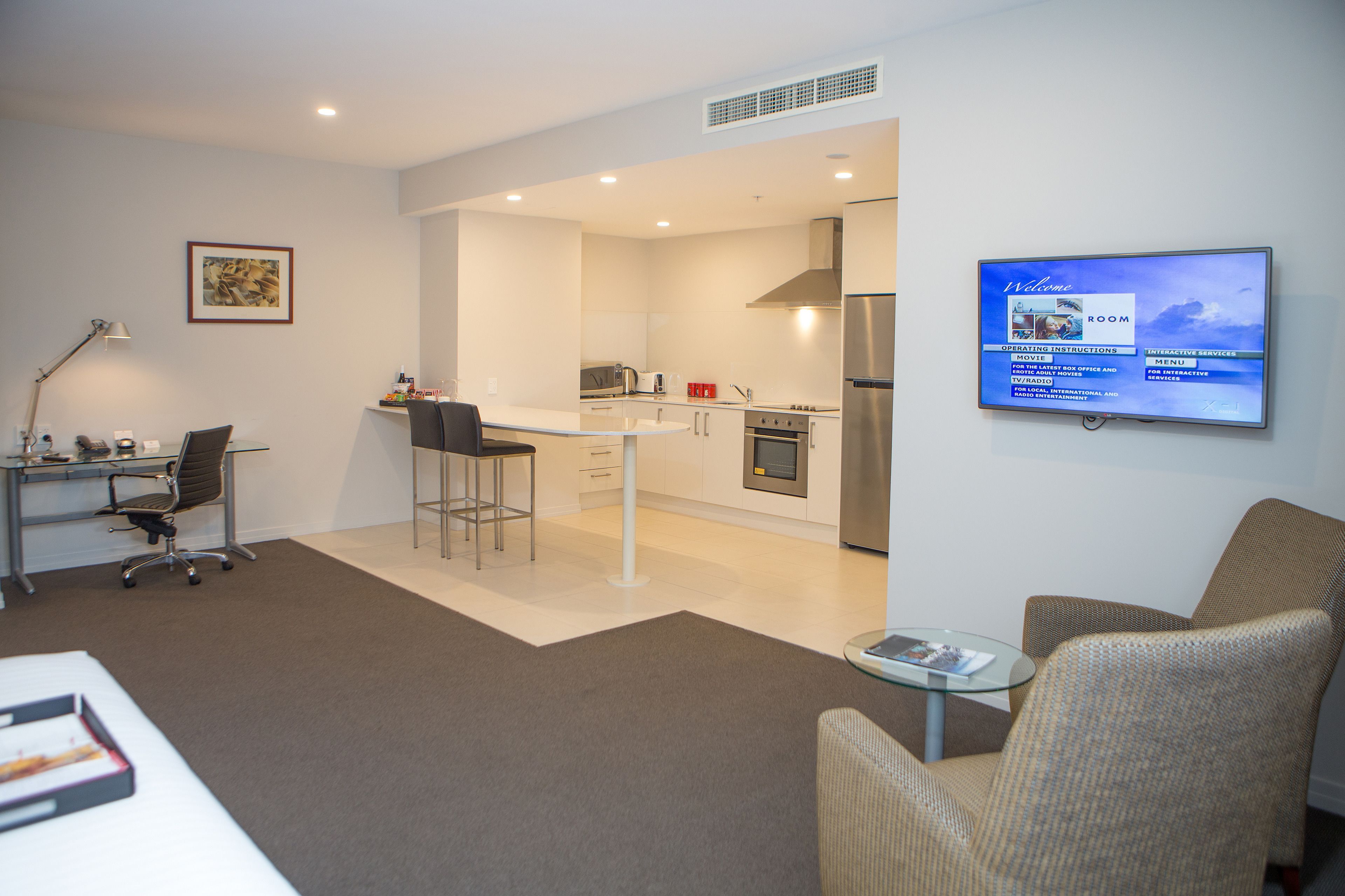 A modern hotel room with a kitchenette, a dining area, and a living space.