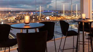 A high-rise room with a panoramic city view, featuring a table with a candle and chairs. - Rydges Auckland (Auckland)
