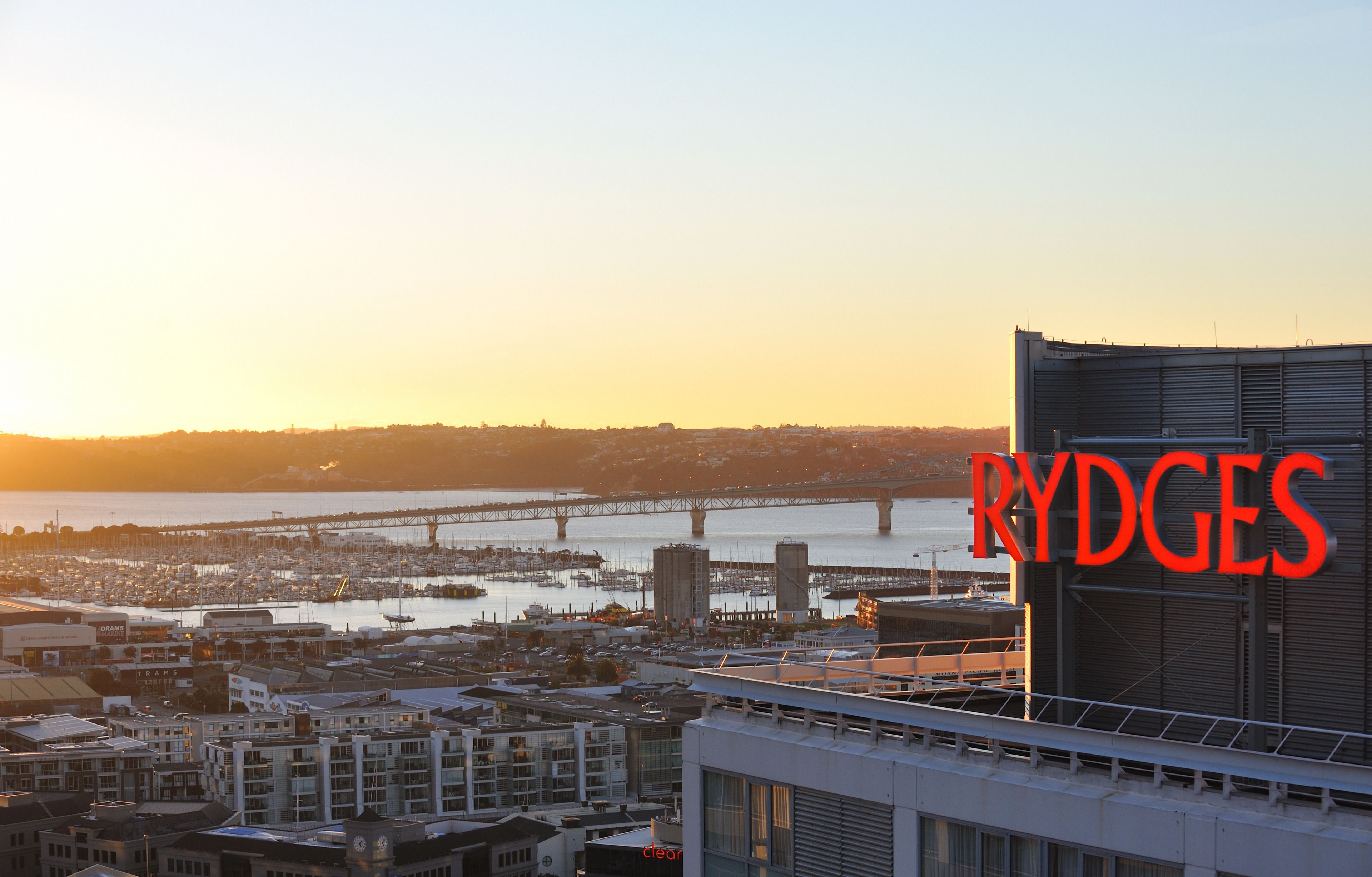 Eine Stadtansicht mit einem markanten Gebäude mit der Aufschrift "RYDGES" und einer Brücke im Hintergrund.