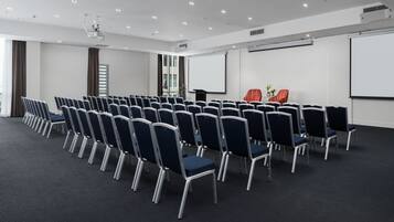 A conference room with rows of chairs, a projector, and a screen.