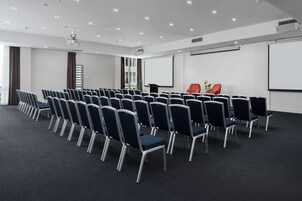 A conference room with rows of chairs, a projector, and a screen.