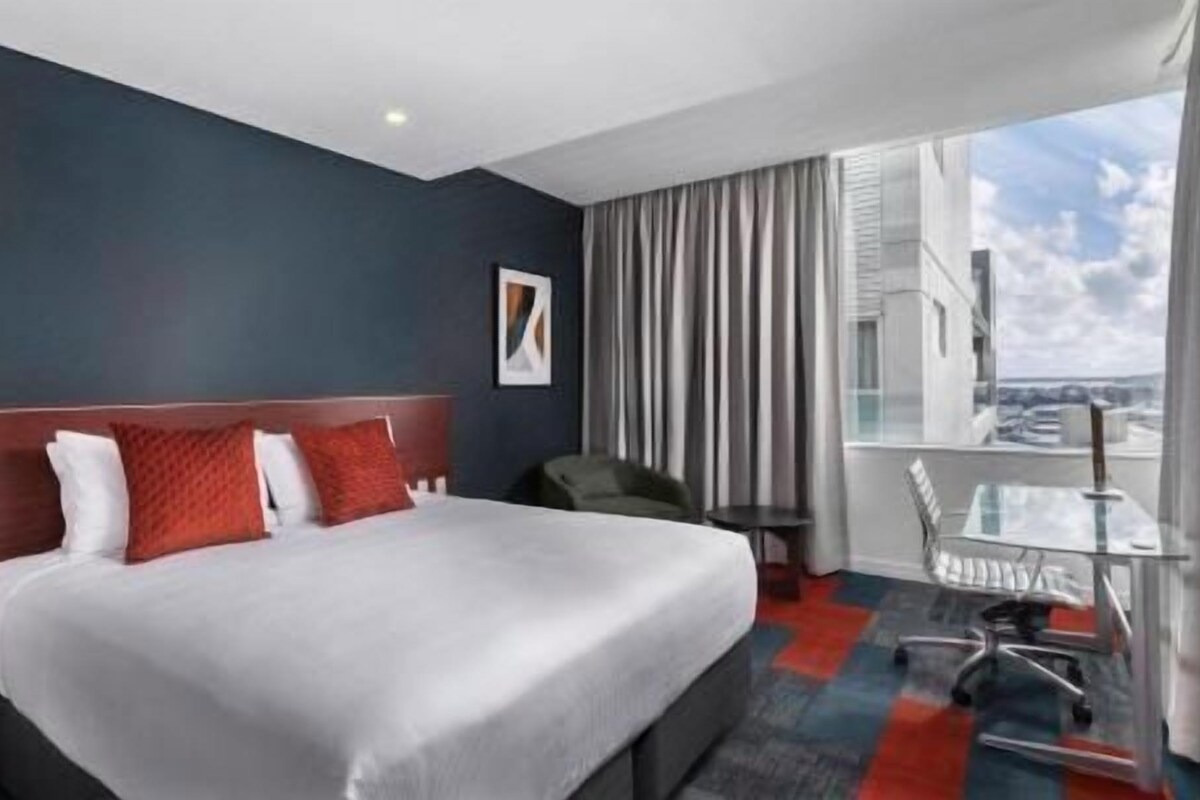 A hotel room with a bed, a desk, and a view of the city.