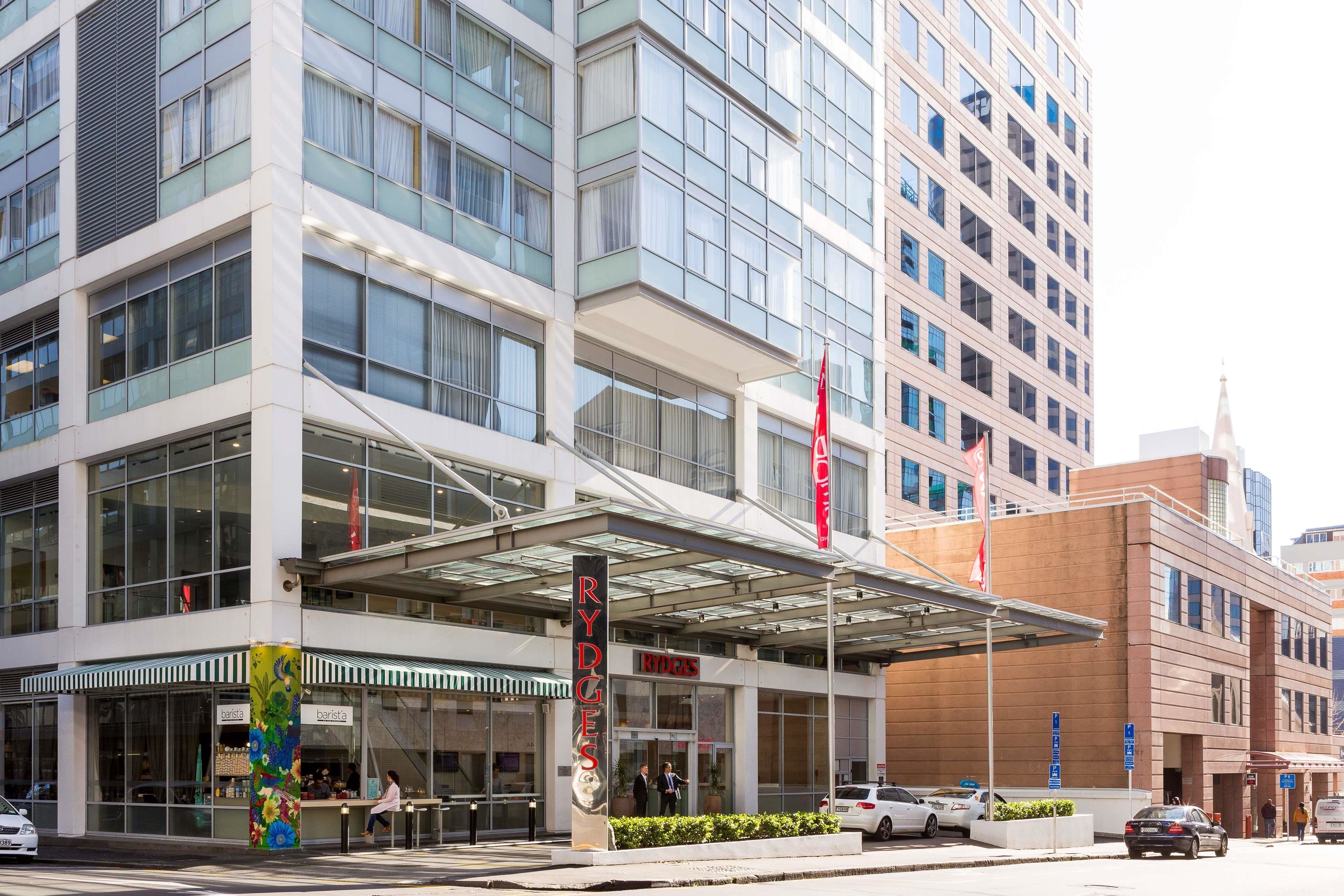 A modern hotel with a glass facade, a covered entrance, and a flagpole.
