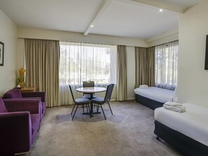 A hotel room with a bed, a desk with chairs, a sofa, and large windows with curtains. - Mercure North Melbourne (North Melbourne)