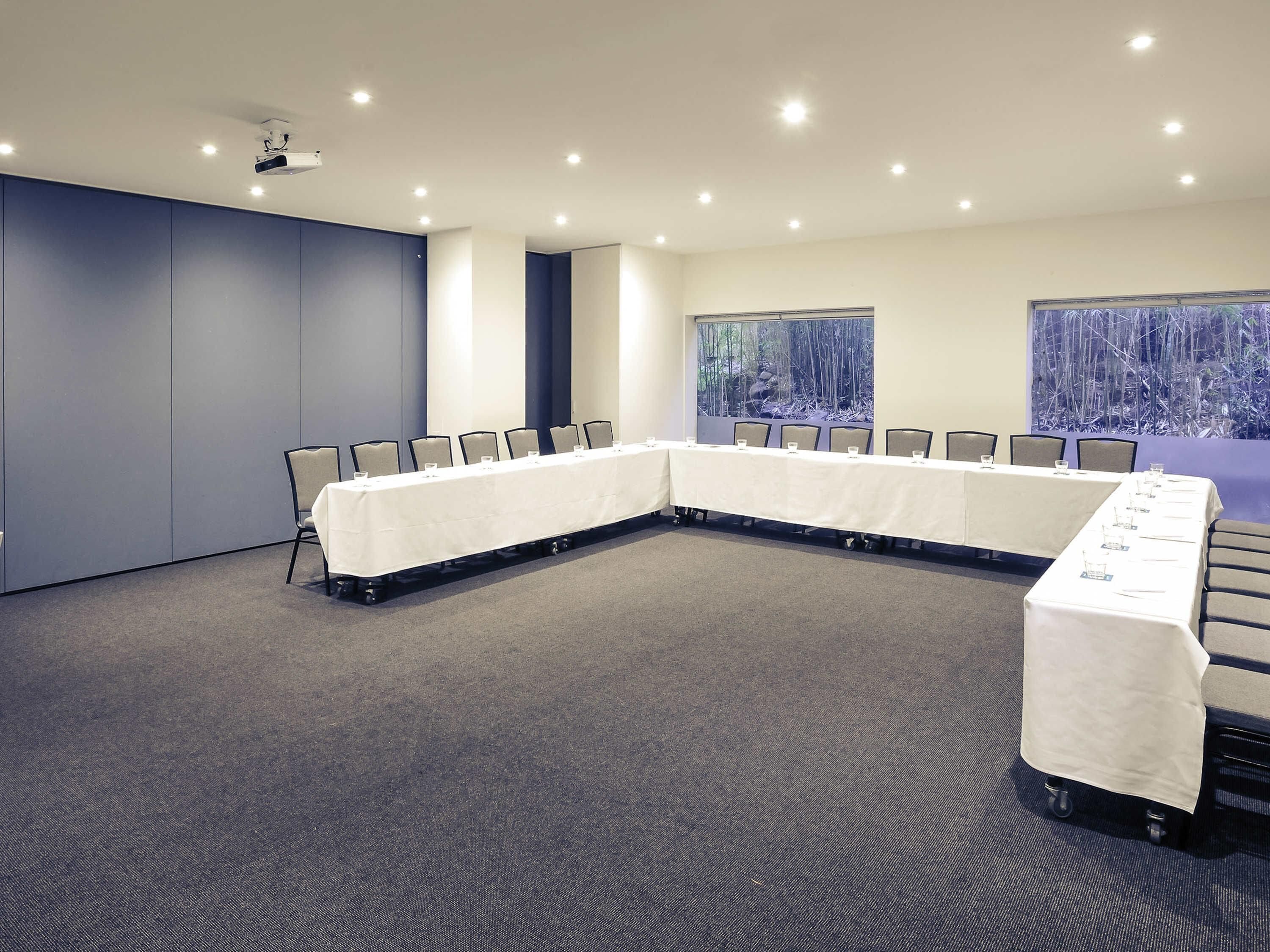 Un salón de conferencias con una larga mesa, sillas y un proyector.