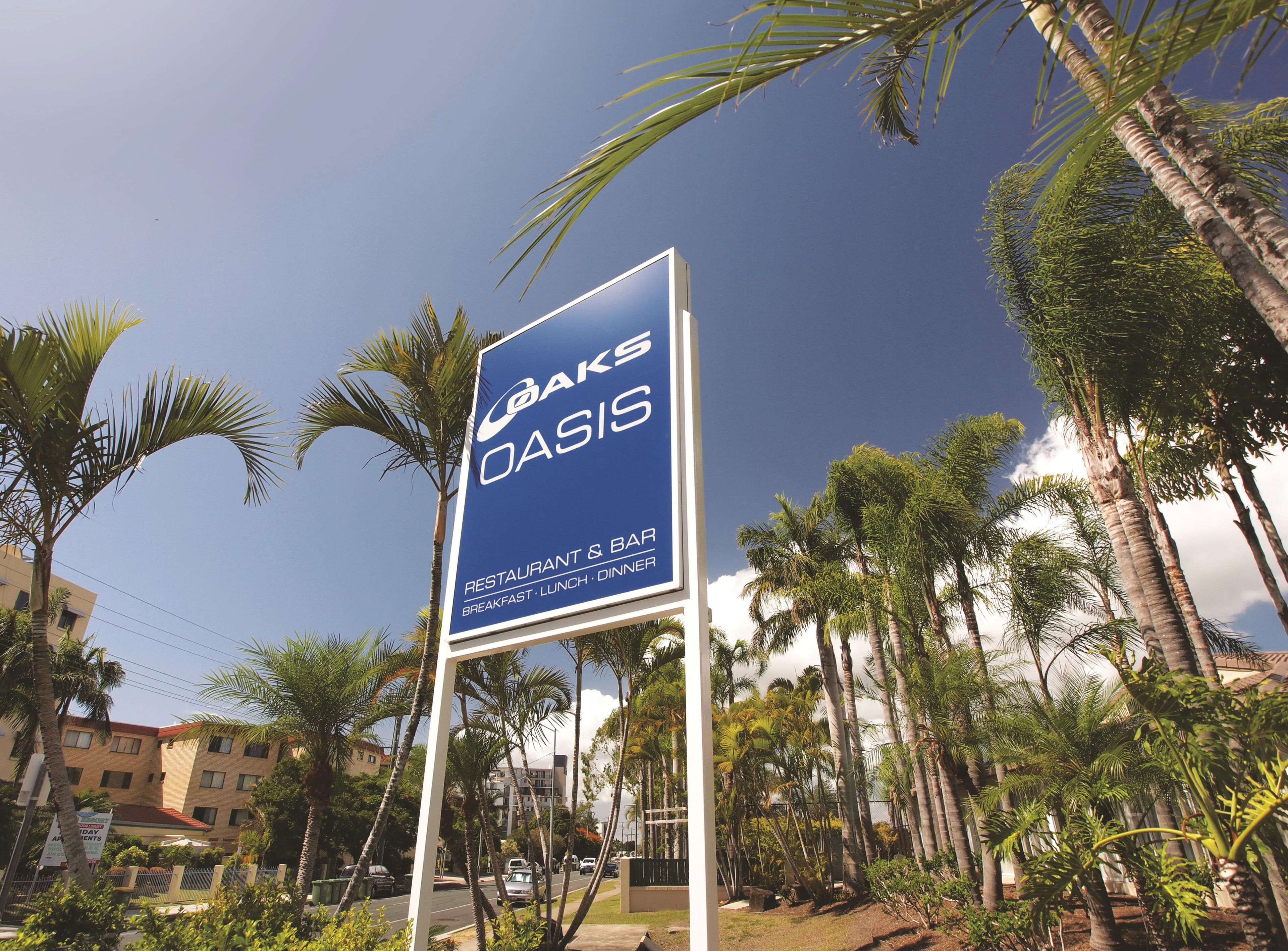 Señal de 'OAKS OASIS' que indica un restaurante y bar con servicio de desayuno, comida y cena.