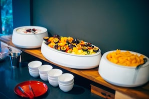 Una mesa de buffet con diversos platos, incluyendo frutas, verduras y un plato rojo con cubiertos.