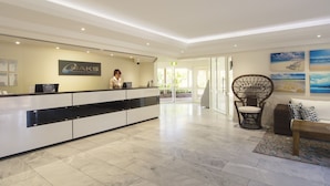 Een hotel receptie met een modern design, met een receptiebalie, een zithoek met een rieten stoel, en kunstwerken aan de muren.