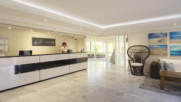 Een hotel receptie met een modern design, met een receptiebalie, een zithoek met een rieten stoel, en kunstwerken aan de muren.