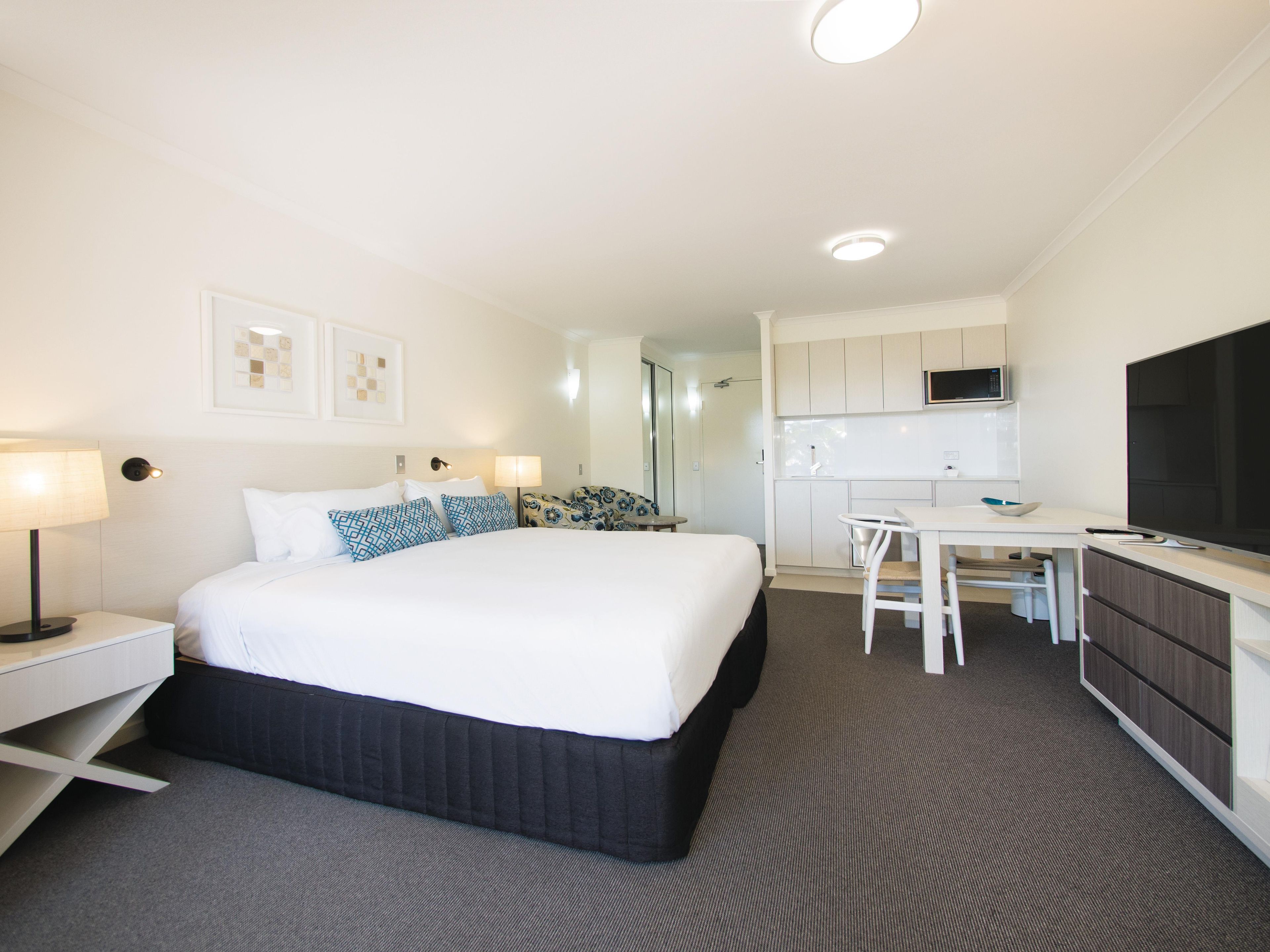 A hotel room with a bed, bedside tables, a desk, a chair, a microwave, and a television.