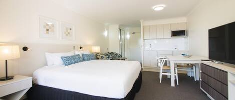 A hotel room with a bed, bedside tables, a desk, a chair, a microwave, and a television.