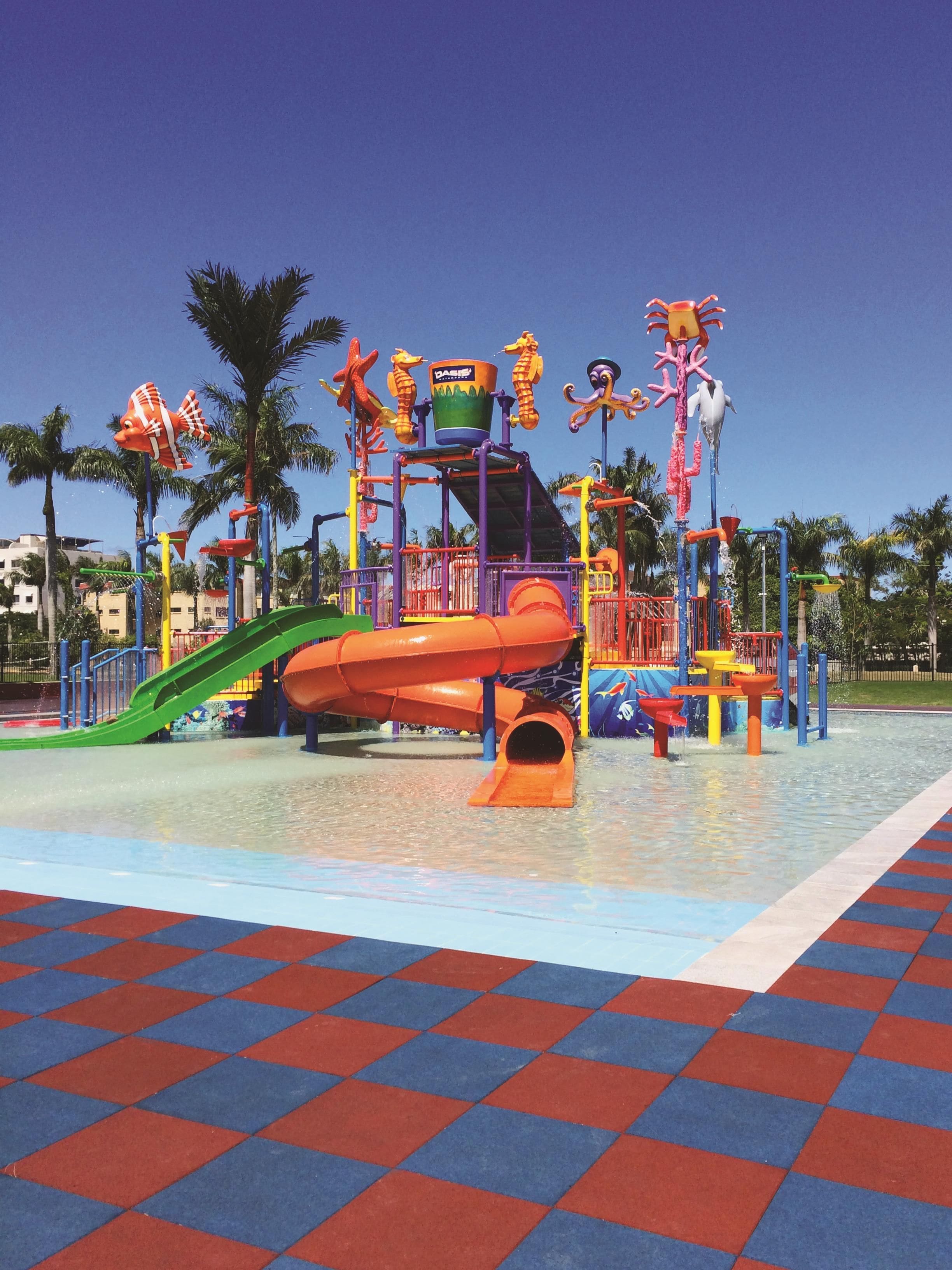 Parque acuático con un tobogán naranja grande, varias atracciones acuáticas y un suelo a cuadros.