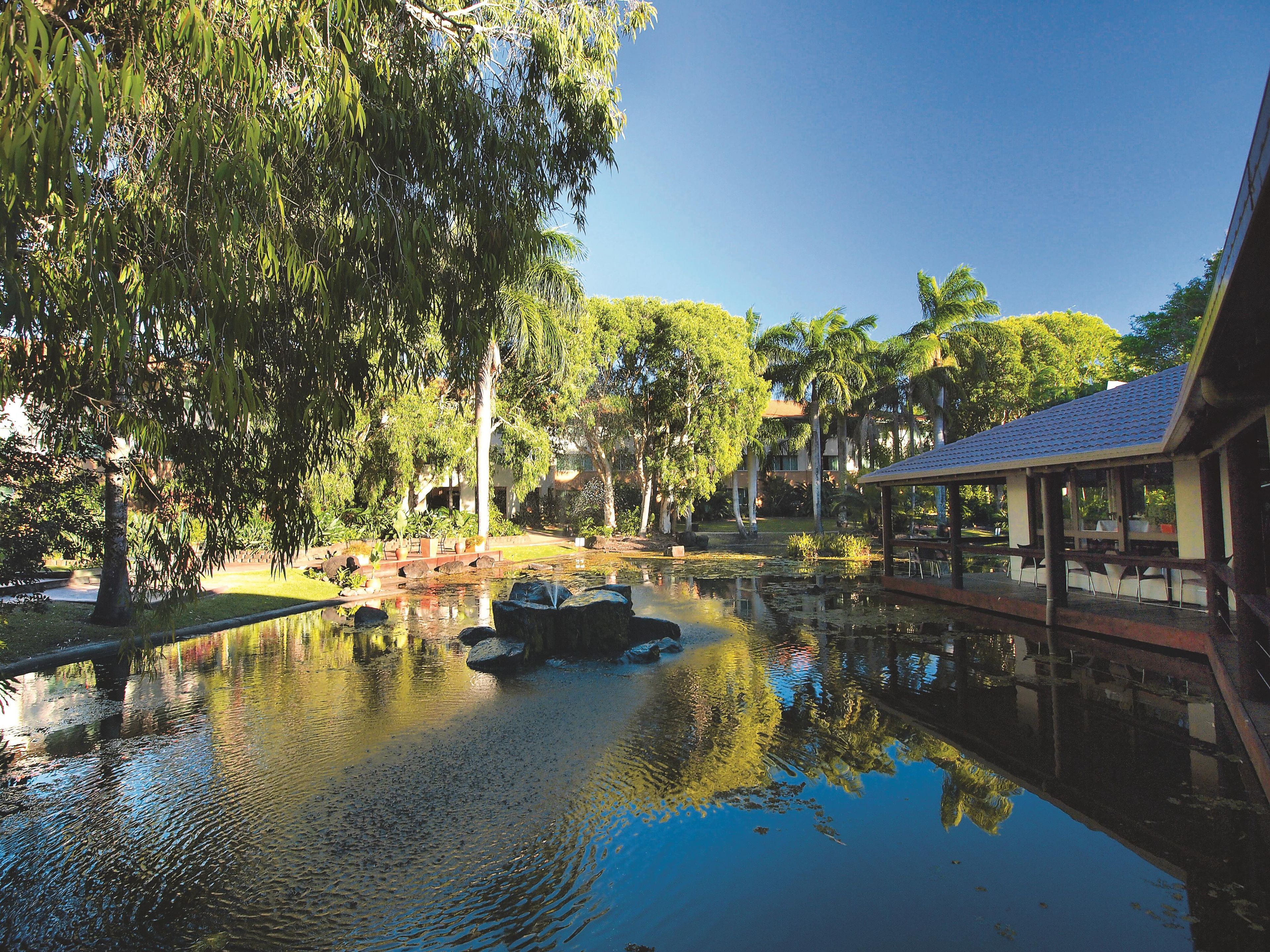 A tranquil outdoor area with a pond, trees, and a covered seating area.