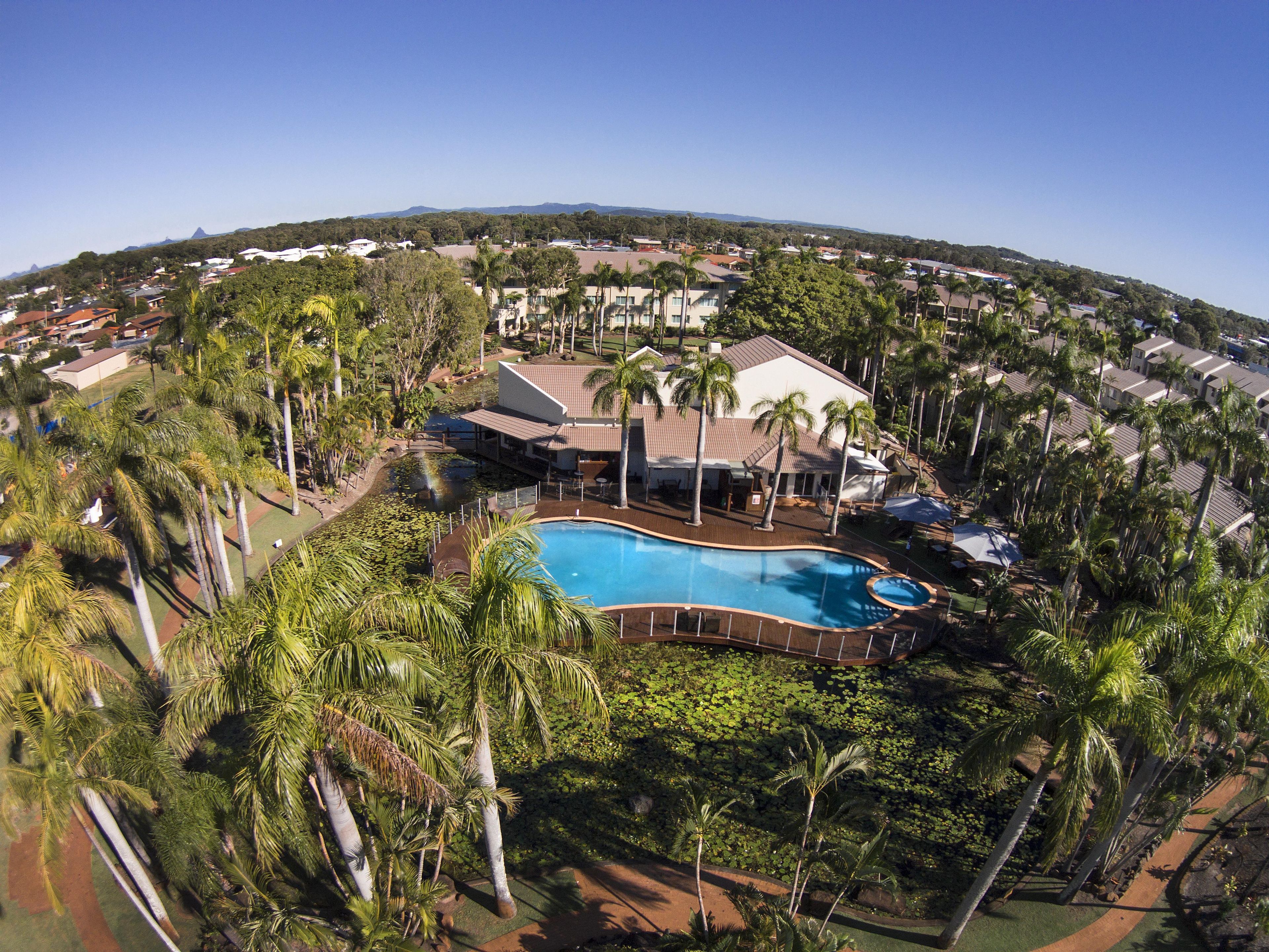 A resort with a swimming pool surrounded by palm trees and a view of the surrounding neighborhood.