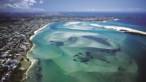 An aerial view of a coastal area with a beach, clear waters, and a densely populated urban area in the background.