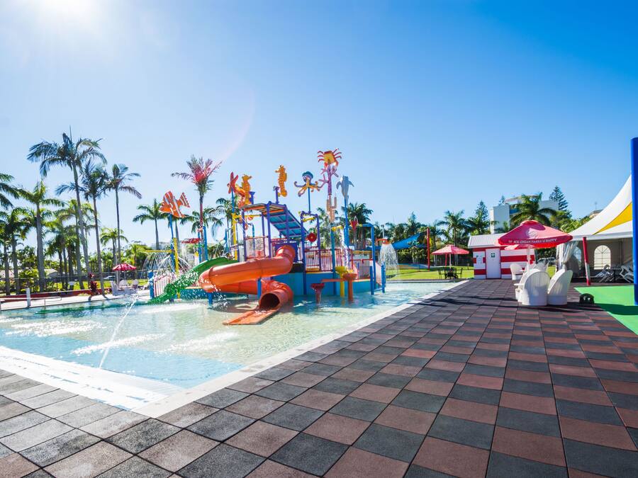 Zona de parque acuático con piscina, toboganes y un pequeño puesto de helados.