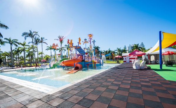 Zona de parque acuático con piscina, toboganes y un pequeño puesto de helados.