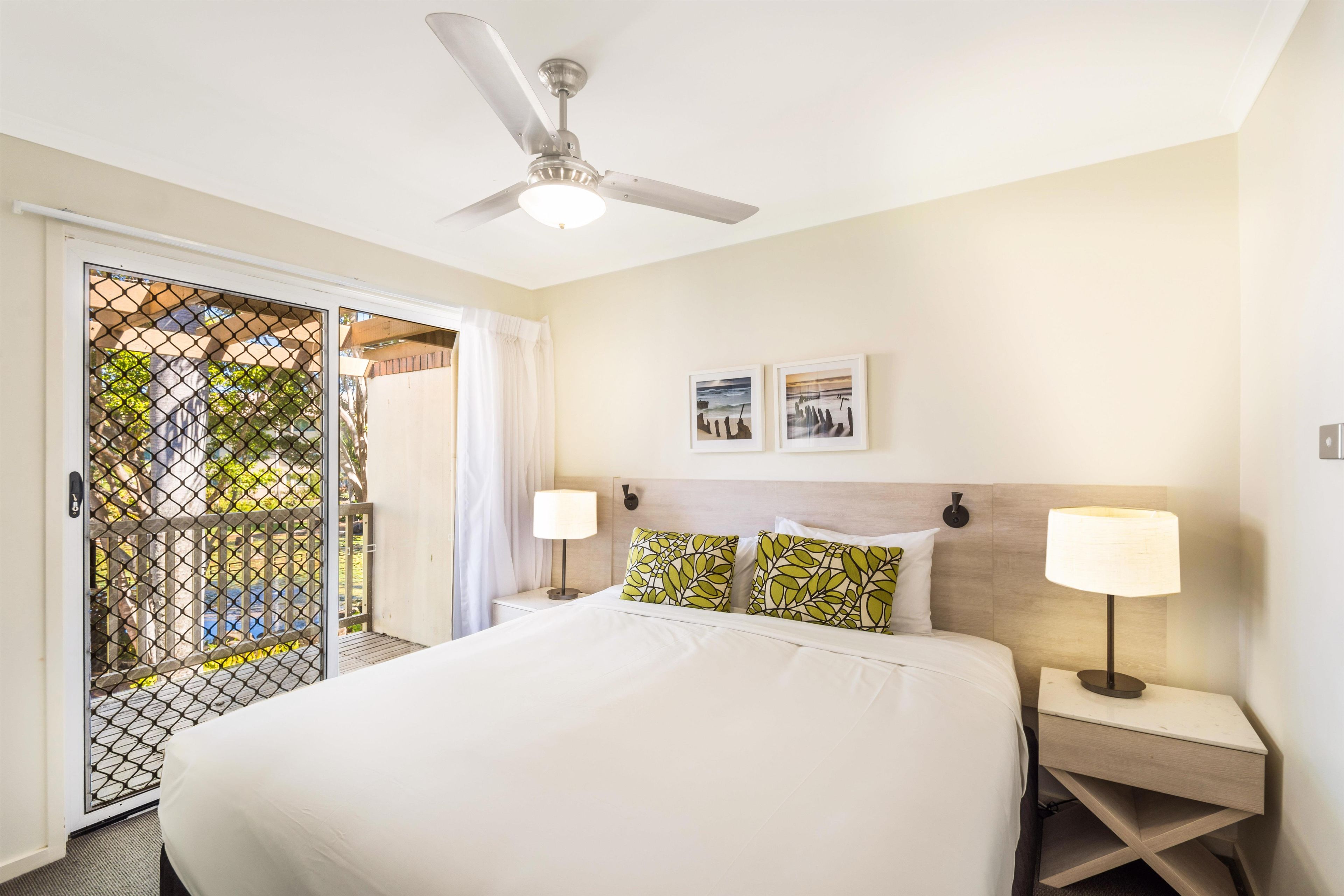 A hotel room with a bed, two nightstands, a ceiling fan, and a view through a door with a mesh screen.