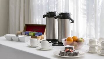 A breakfast setup with coffee makers, cups, a bowl of fruit, and a plate of cake.