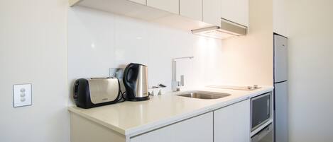 A modern kitchen with white cabinetry, a stainless steel toaster, a kettle, a sink, and a refrigerator.