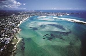 Une vue aérienne d’une ville côtière, avec une plage, des eaux cristallines et, au loin, le profil d’une ville.