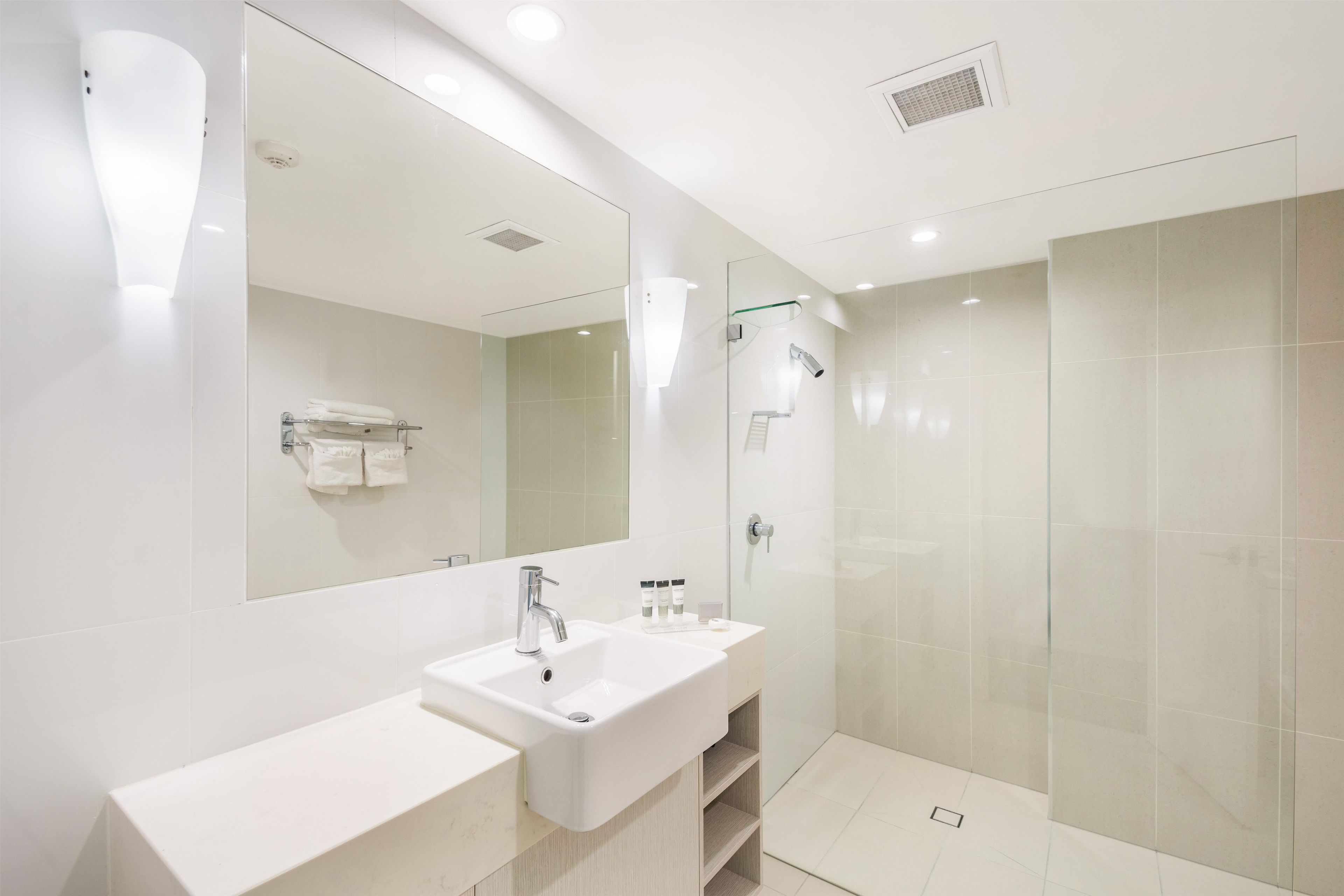 Une salle de bain moderne avec un grand miroir, deux lavabos, une douche et un porte-serviettes.
