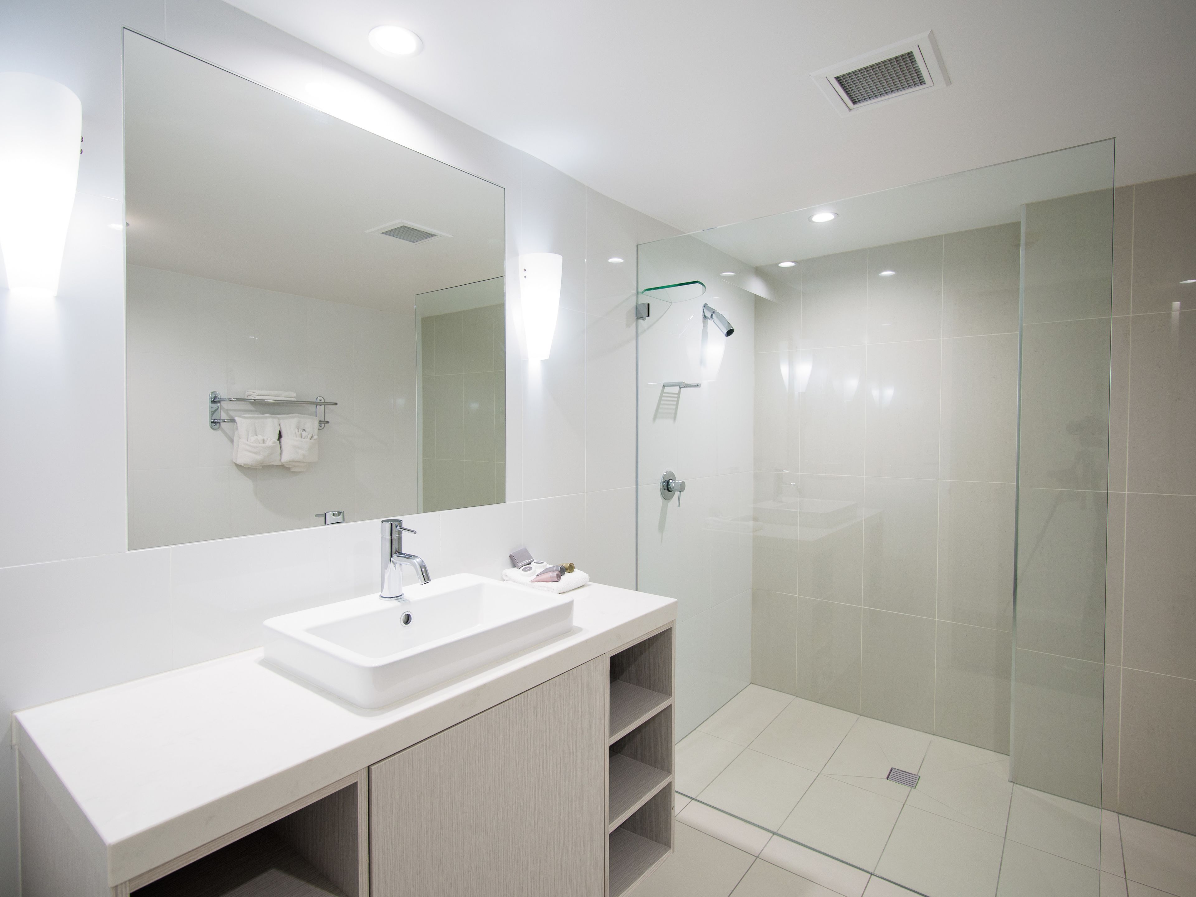 A modern bathroom with a large mirror, a white sink, and a glass-enclosed shower area.