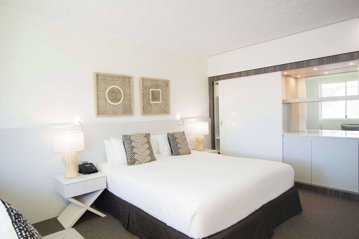 A hotel room with a large bed, two bedside tables, a desk, and a window.