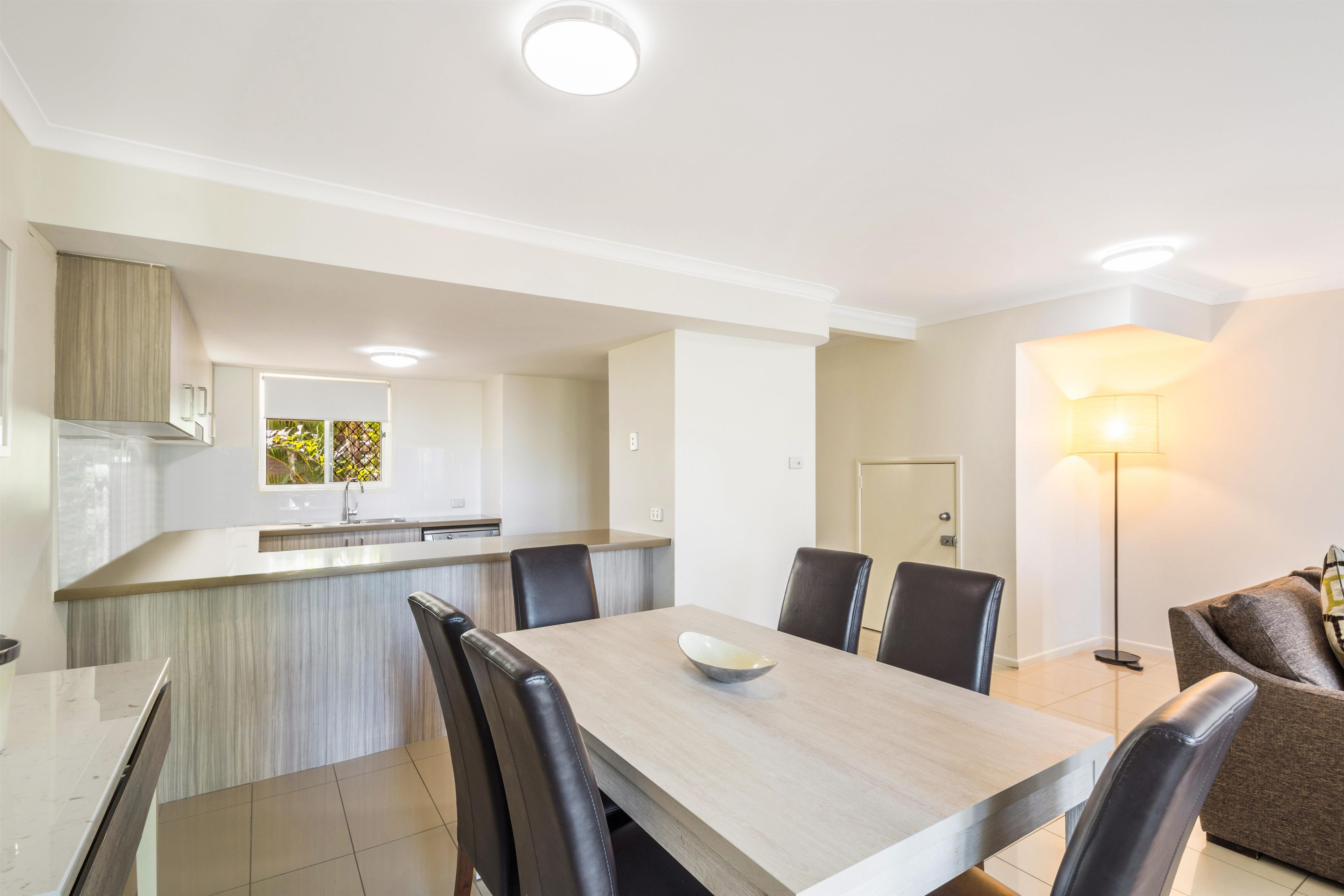 A modern kitchen with a central island, dining area with chairs, and a lamp.