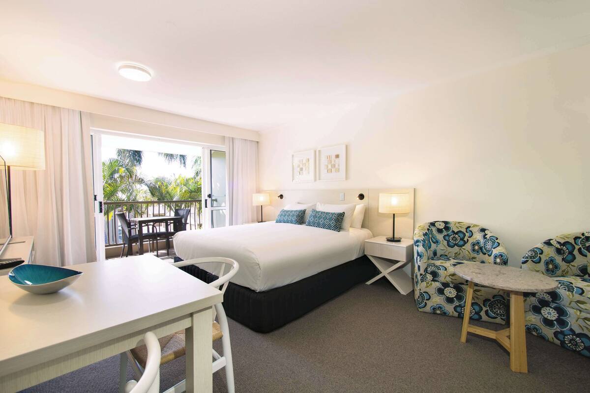 A hotel room with a bed, a desk, a chair, a small table, and a sofa.