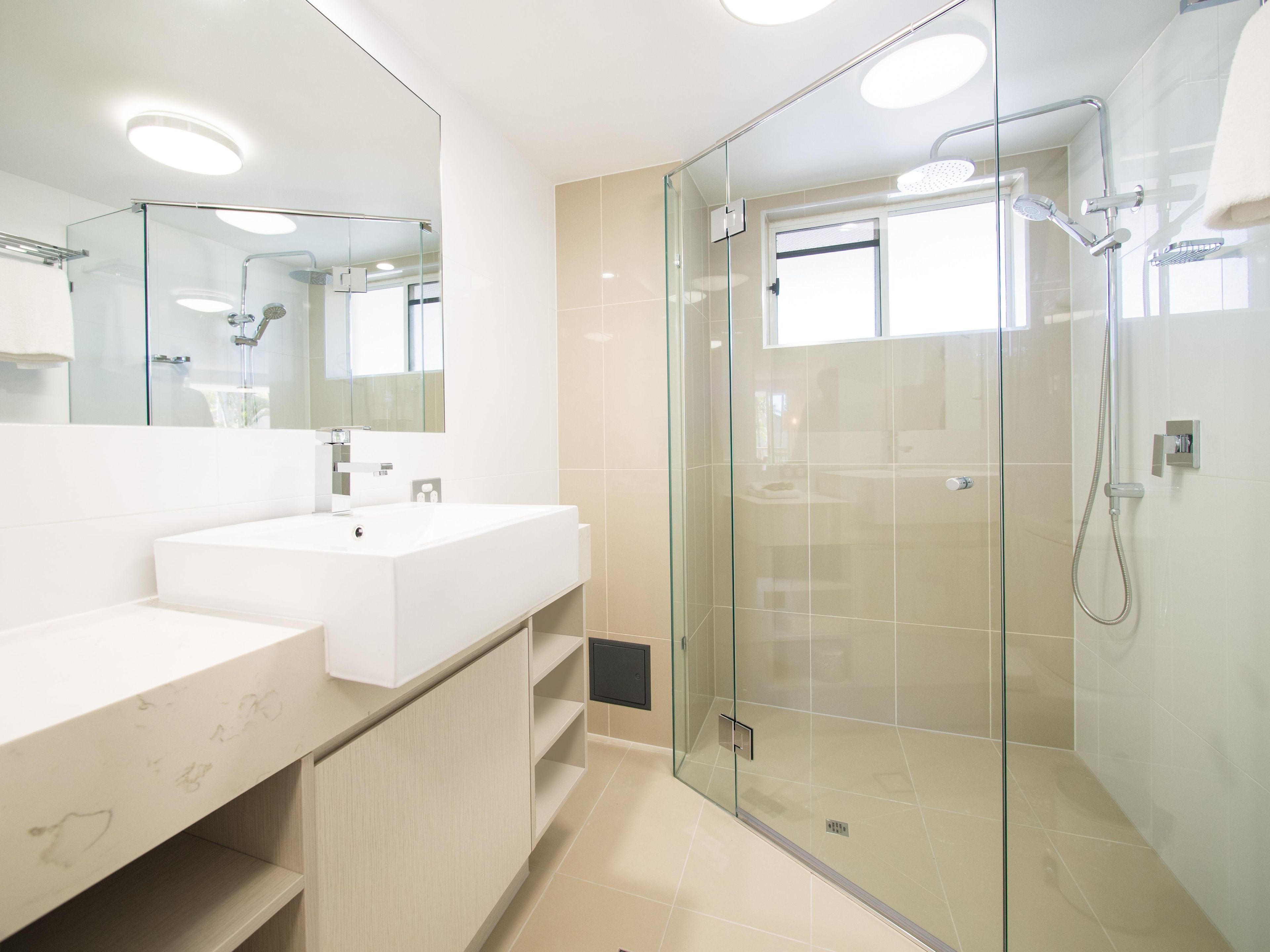 Un baño moderno con ducha acristalada, lavamanos blanco y un espejo grande.