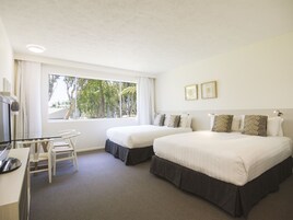 Habitación de hotel con dos camas, un escritorio y una silla. Se ve una ventana con vistas a árboles y un techo con luz empotrada.
