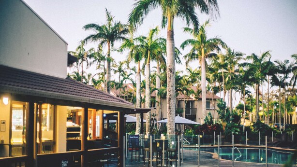 A poolside area with a restaurant, palm trees, and a clear sky.