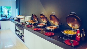 Een buffetopstelling met diverse etenswaren in metalen serveerschaaltjes, gerangschikt op een toonbank met een donkere achterwand.