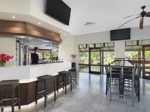 Un espace bar moderne avec un comptoir, des tabourets de bar et un téléviseur fixé au mur.