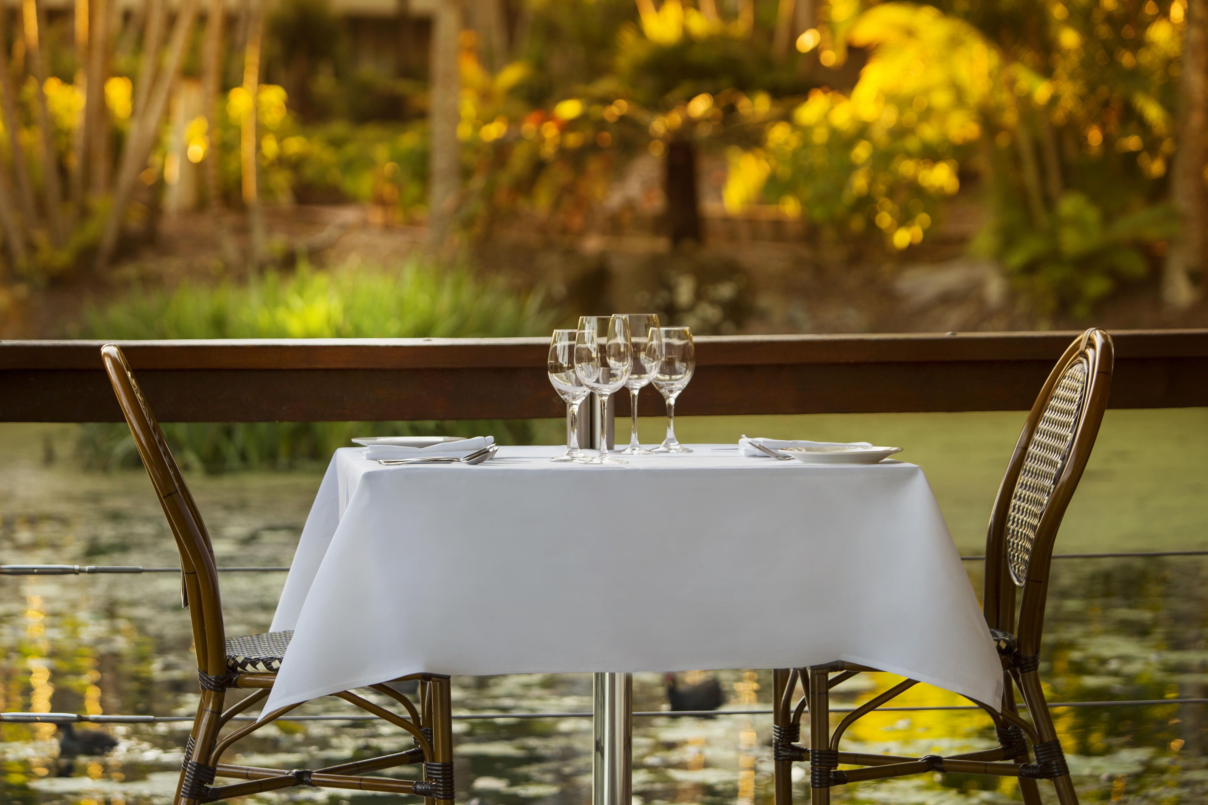 A table set for four with wine glasses, plates, and cutlery, overlooking a water feature.