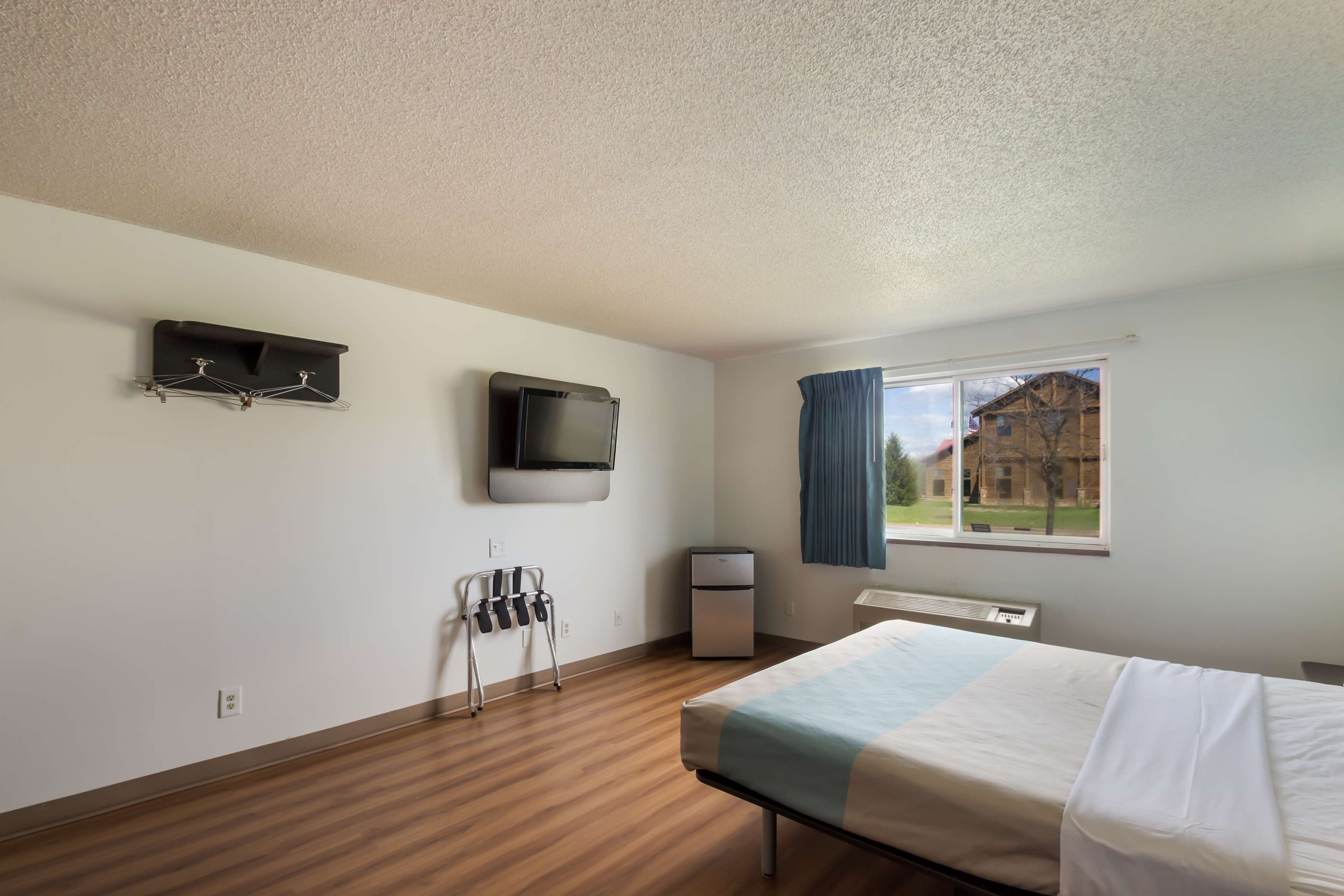 A hotel room with a bed, a television mounted on the wall, a small heater, and a window with curtains.