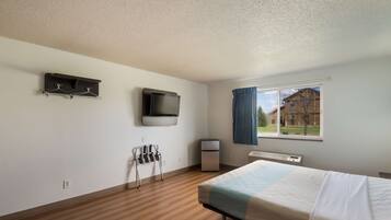 A hotel room with a bed, a television mounted on the wall, a small heater, and a window with curtains.