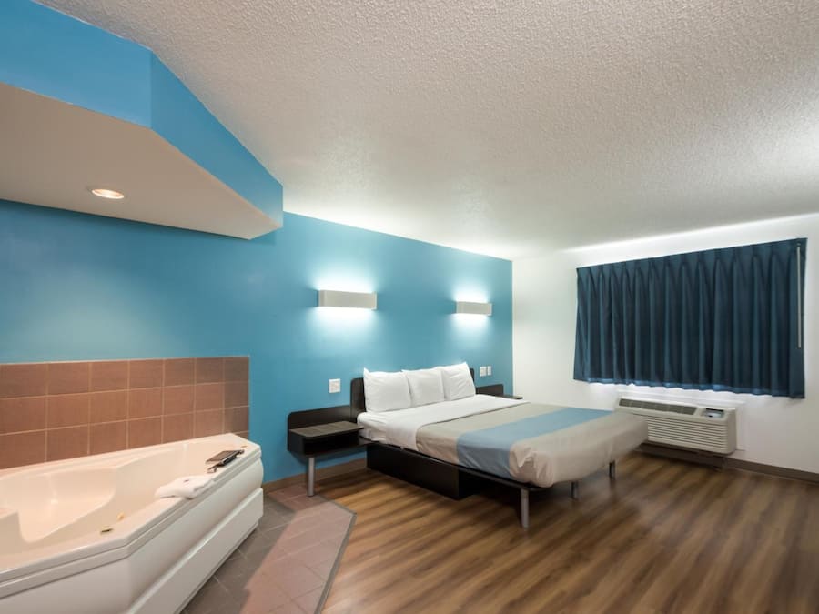 A hotel room with a bed, a bathroom with a bathtub, and a window with curtains.