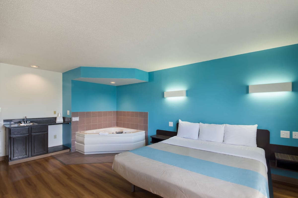 A hotel room with a large bed, a separate bathroom with a bathtub, a kitchenette, and a blue accent wall.