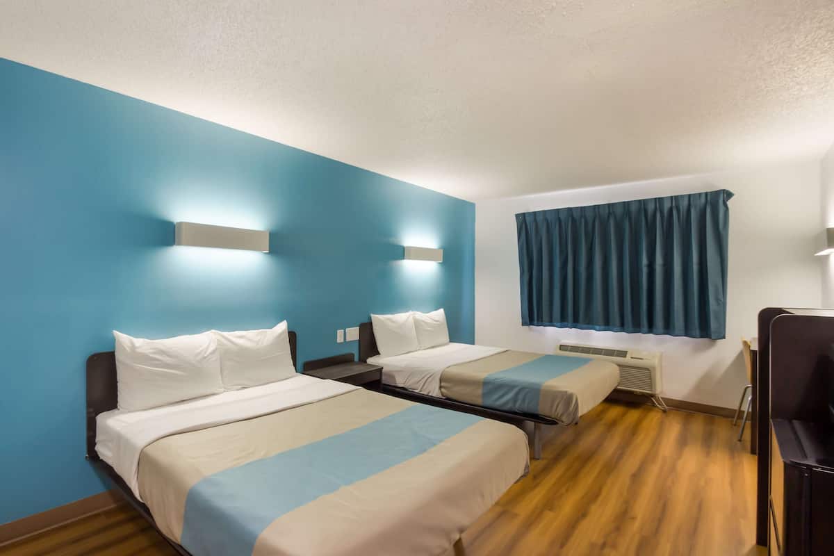 A hotel room with two beds, a desk, and a window with curtains.