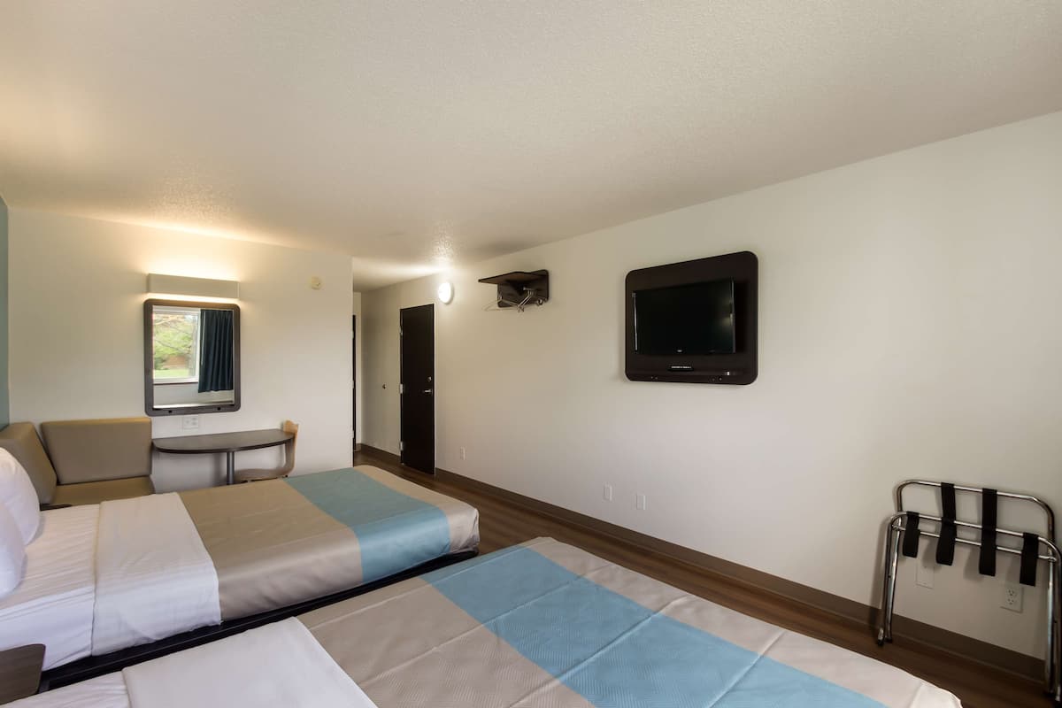 A hotel room with two beds, a desk, a chair, a TV, and a window with curtains.