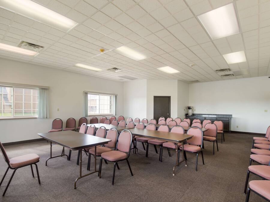 Uma sala de conferências com várias mesas e cadeiras, grandes janelas e uma pequena cozinha.