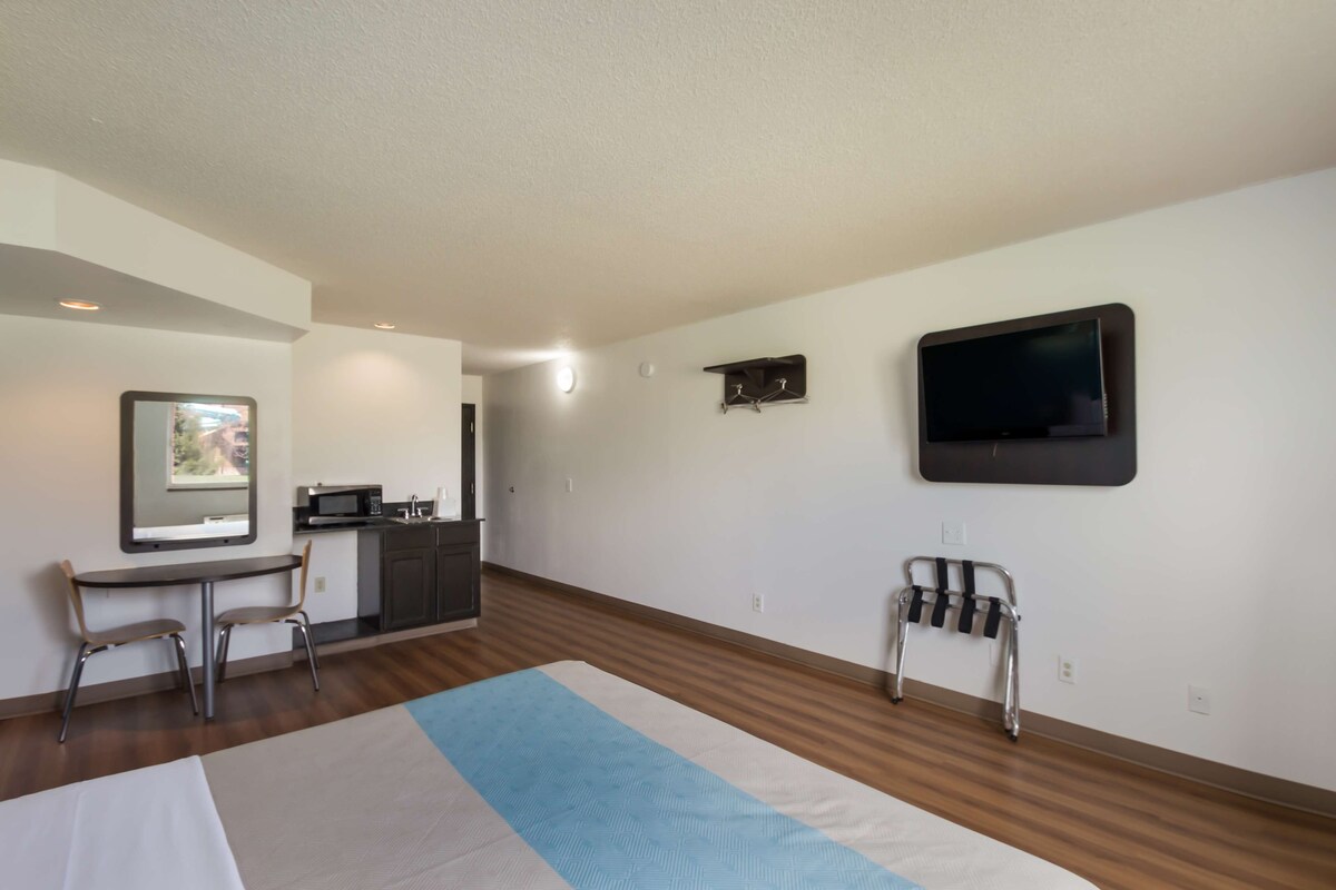 Une chambre d’hôtel moderne équipée d’une kitchenette, d’un téléviseur à écran plat fixé au mur, d’un fauteuil roulant et d’un grand lit.