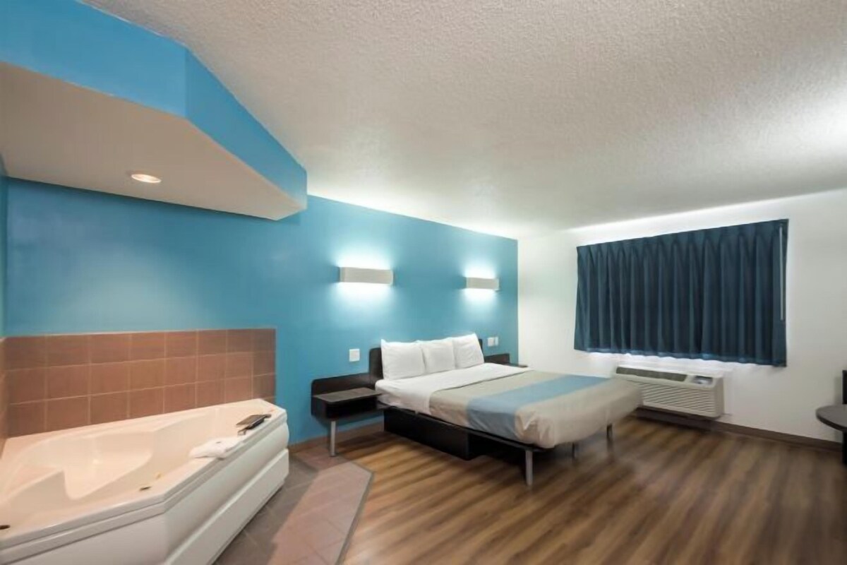 A hotel room with a bed, a bathroom with a bathtub, and a window with curtains.