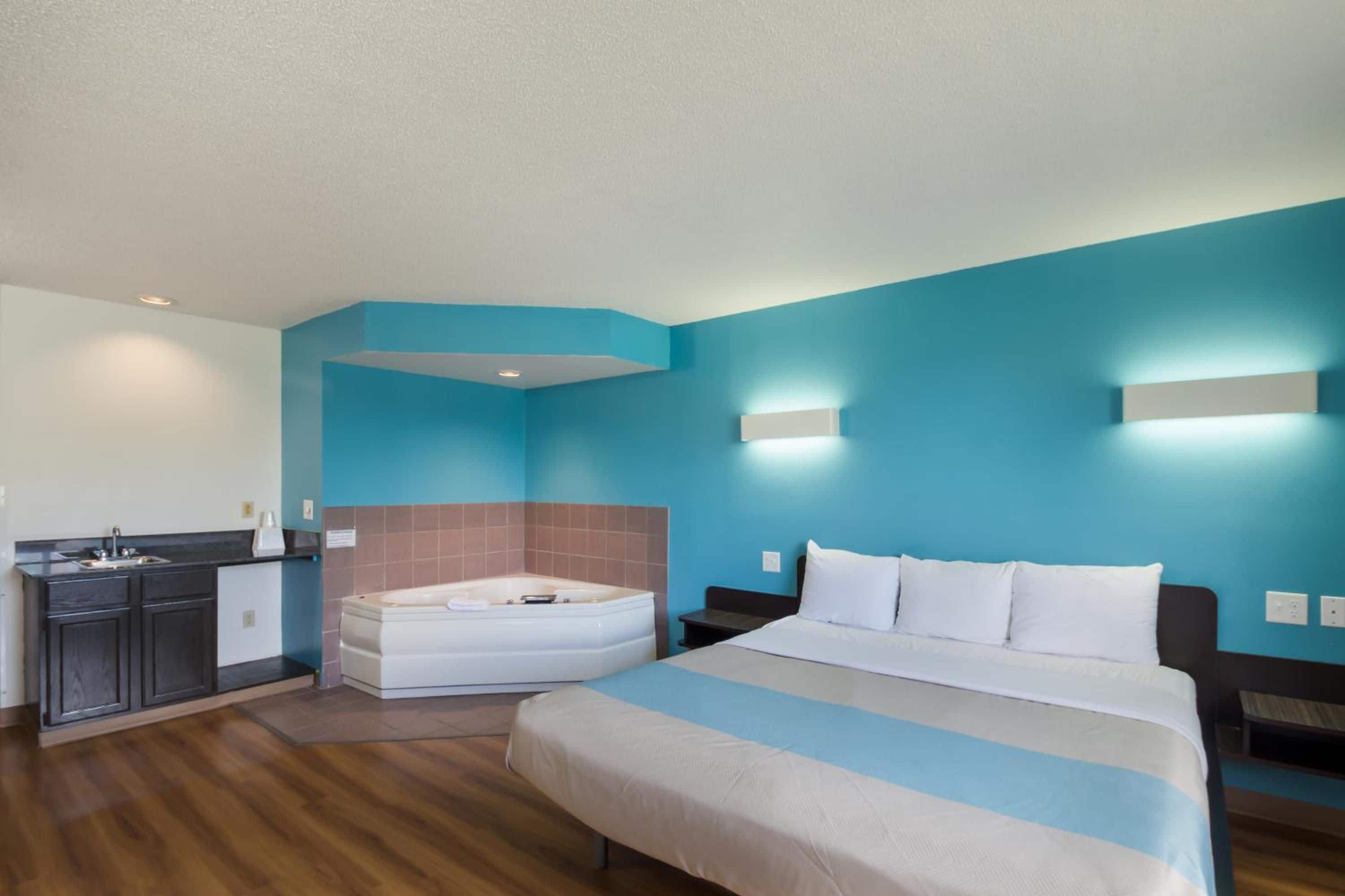 Habitación de hotel con cama, baño con bañera, kitchenette y pared azul.