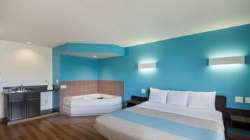 A hotel room with a bed, a bathroom with a bathtub, a kitchenette, and a blue wall.